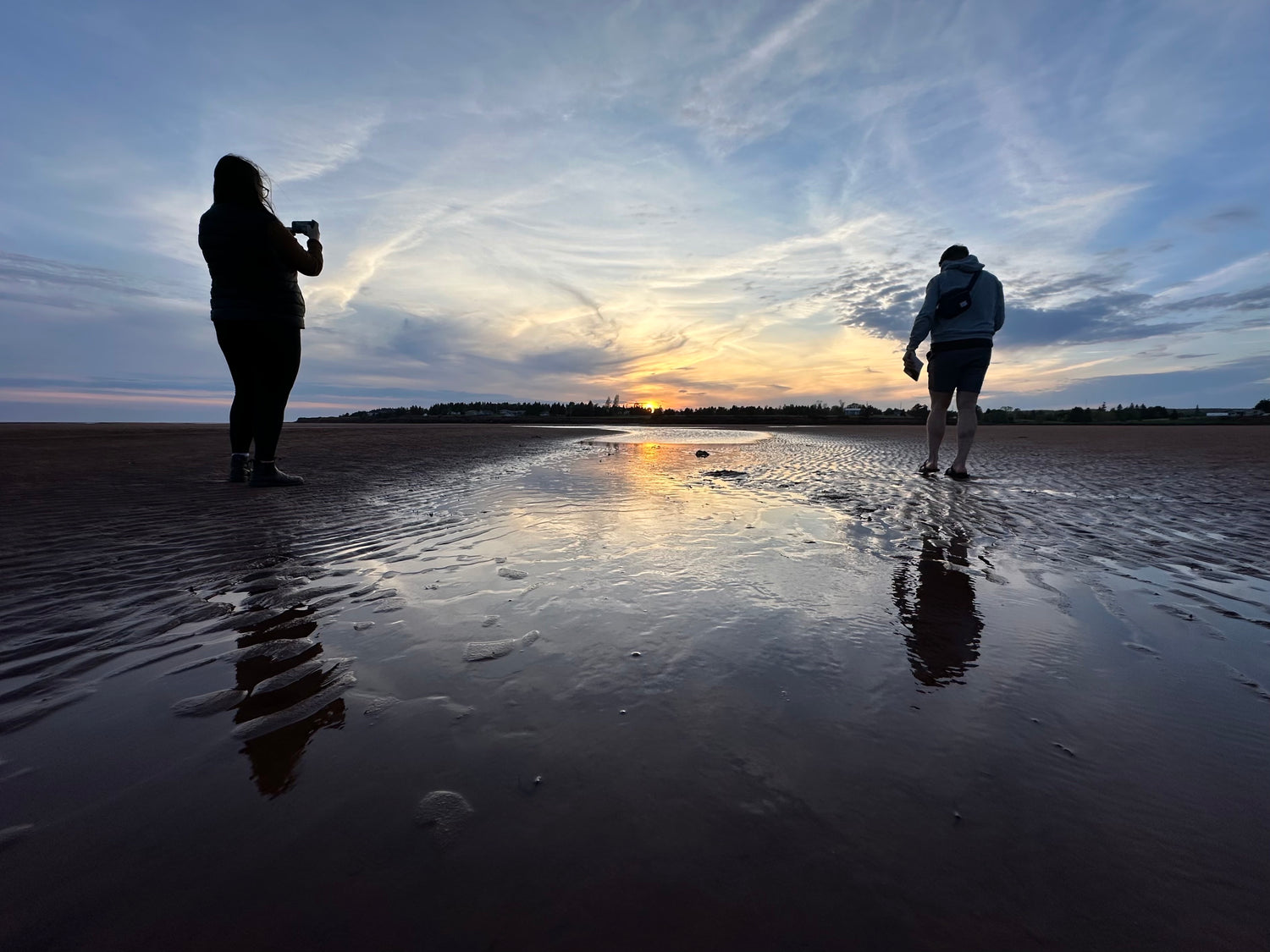 photo of the founders or Red Earth Adventures walking on a beach at low tide looking at the sun setting.