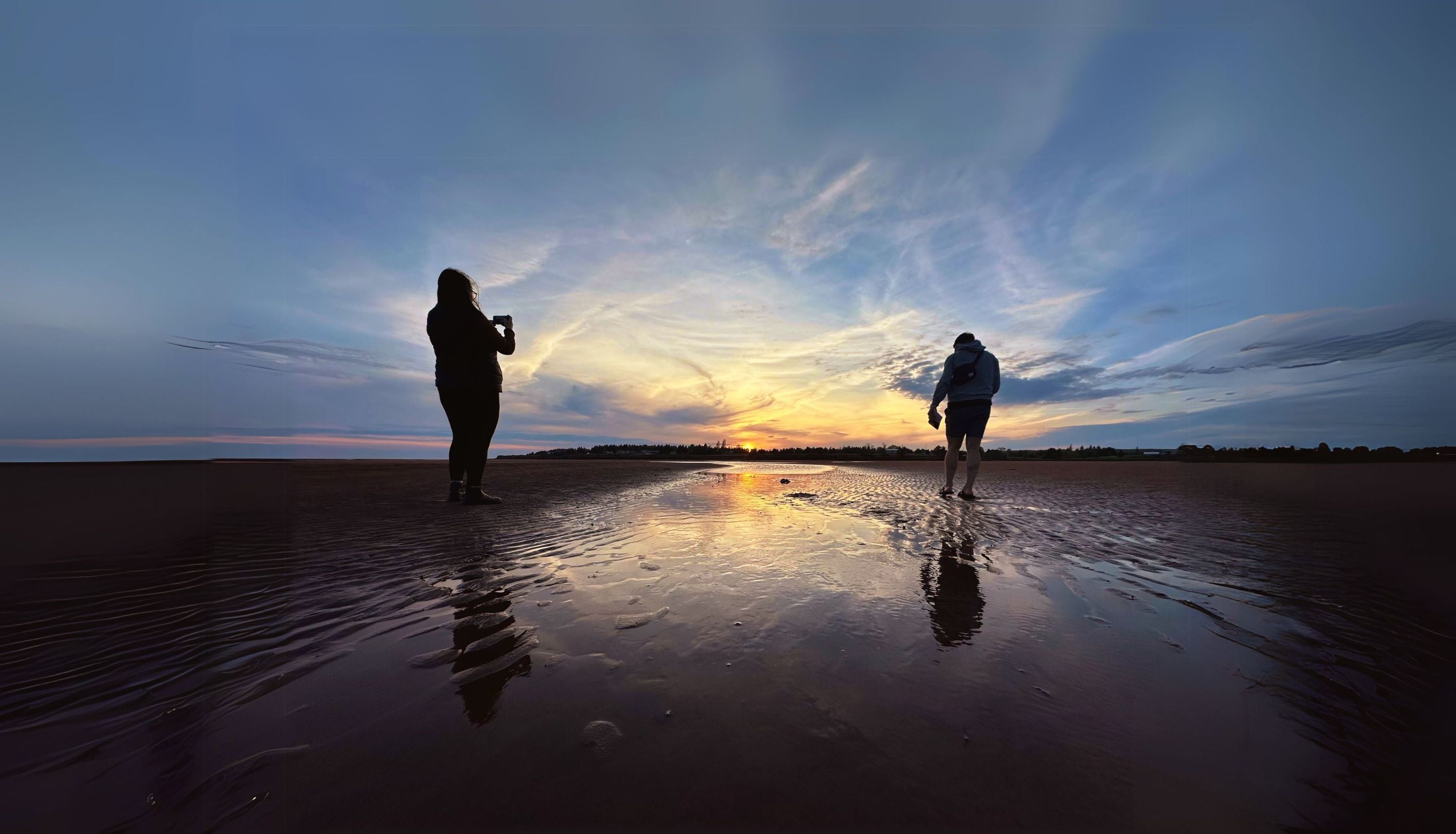 Founders of Red Earth Adventures walking on a beach at low tide taking photos of the sun setting.